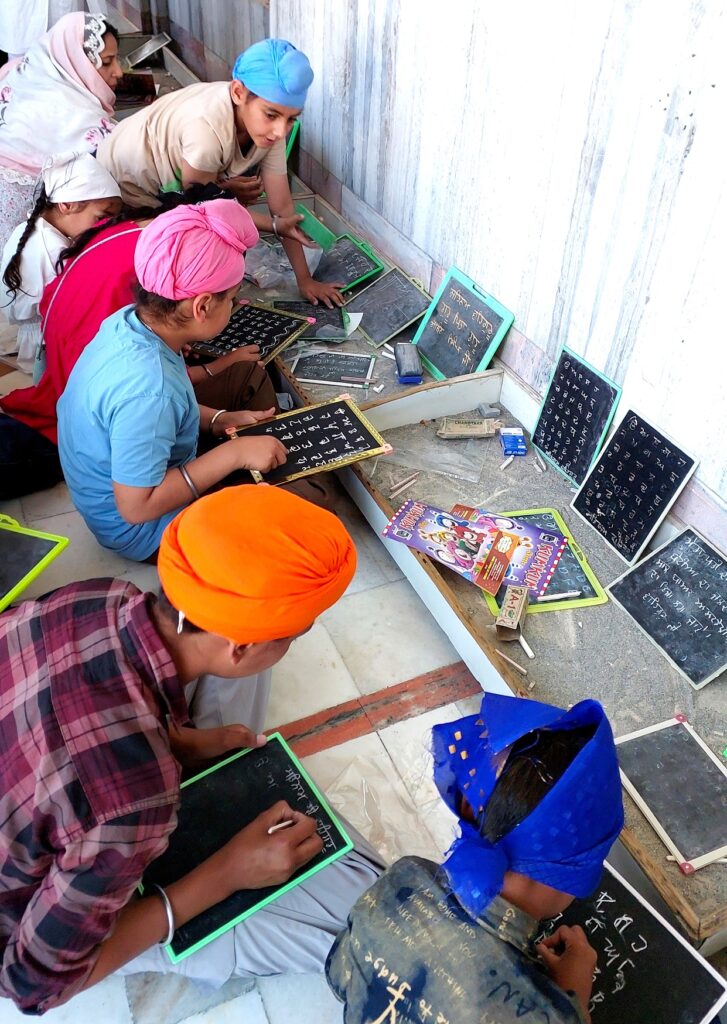 Children write Gurmukhi alphabets on slates in Gurdwara Likhansar Sahib