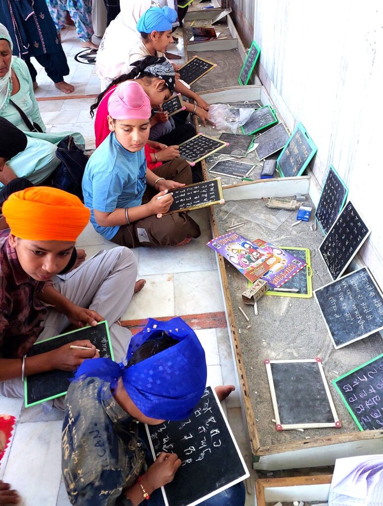 Children write Gurmukhi alphabets on slates in Gurdwara Likhansar Sahib..